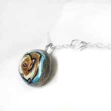 Load image into Gallery viewer, a small beach stone hand painted with a portrait of a guinea pig against a blue background. Available as a keepsake stone or pendant necklace
