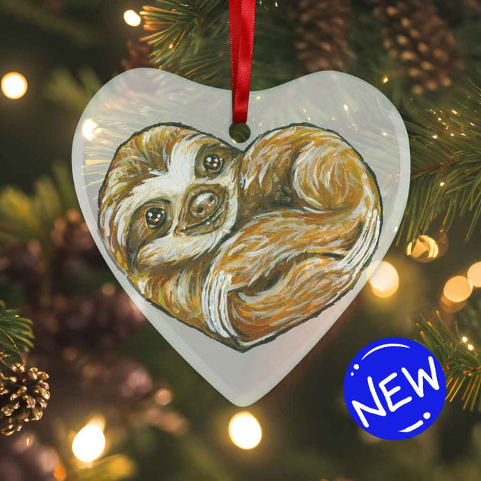 a heart shaped glass ornament, featuring an illustration of a sloth, curled up in the shape of a heart 