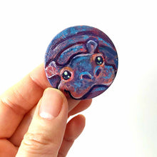 Load image into Gallery viewer, a small smooth wood disc, hand painted with the portrait of a smiling hippopotamus. available as a wood keepsake or pendant necklace 
