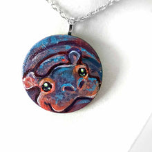 Load image into Gallery viewer, a small smooth wood disc, hand painted with the portrait of a smiling hippopotamus. available as a wood keepsake or pendant necklace 
