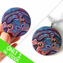 Load image into Gallery viewer, a small smooth wood disc, hand painted with the portrait of a smiling hippopotamus. available as a wood keepsake or pendant necklace 
