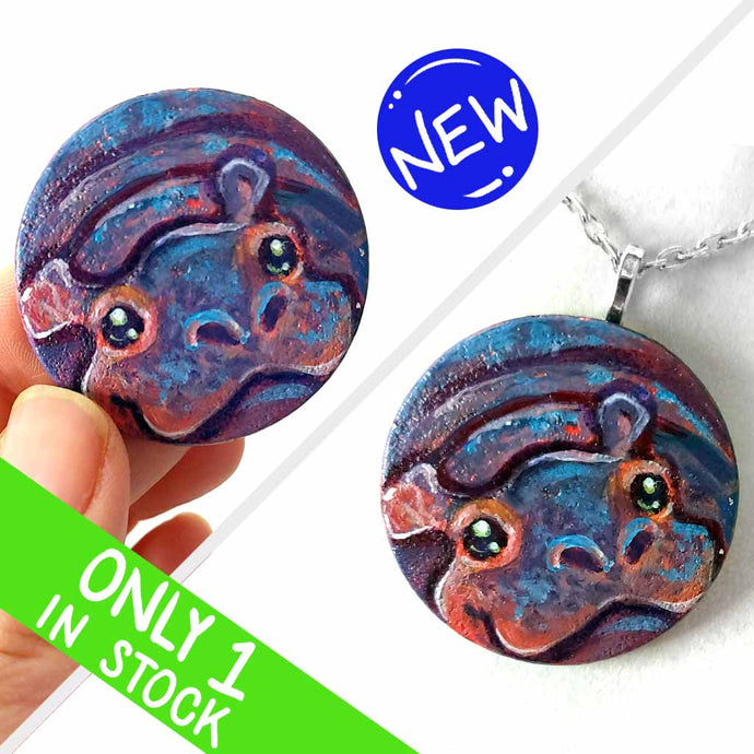a small smooth wood disc, hand painted with the portrait of a smiling hippopotamus. available as a wood keepsake or pendant necklace 