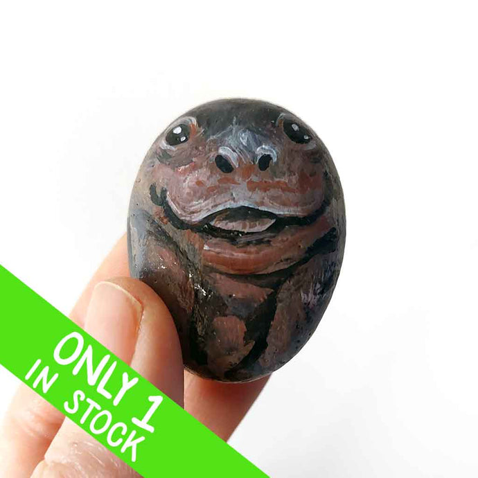 a small beach stone painted to looke like a smiling baby hippo