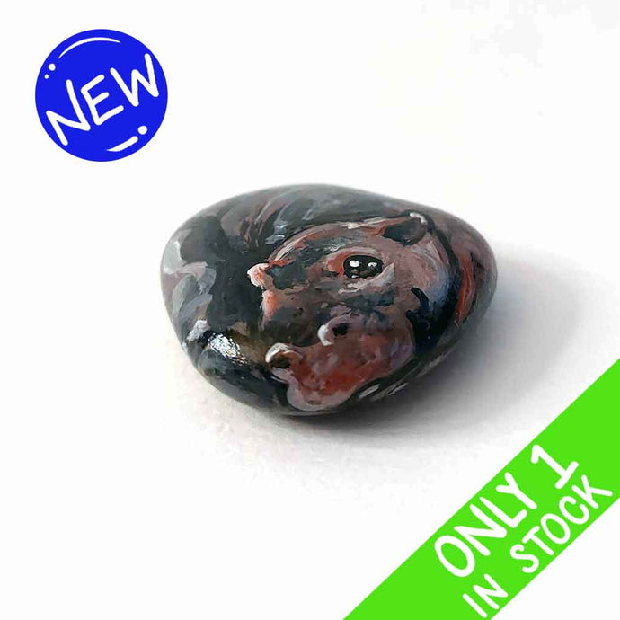 a smooth, flat, beach stone hand painted with a smiling hippopotamus