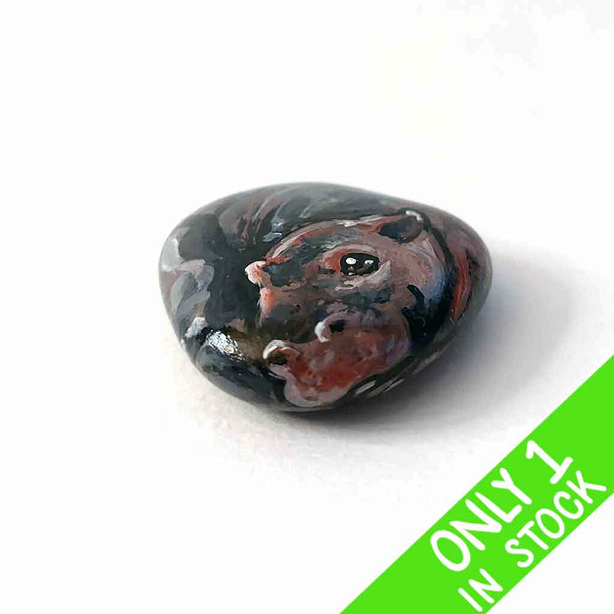 a smooth, flat, beach stone hand painted with a smiling hippo