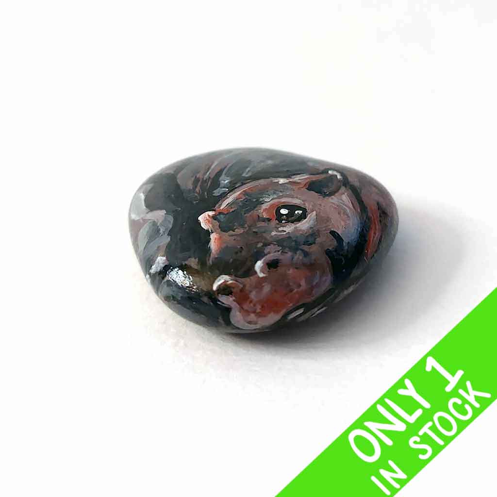 a smooth, flat, beach stone hand painted with a smiling hippo