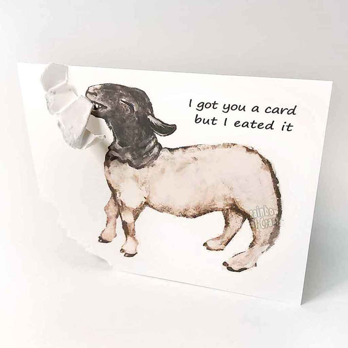 a funny greeting card with a black and white sheep on the front, with the bottom left corner of the card ripped and hanging from its mouth. the card reads, 