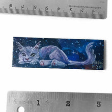 Load image into Gallery viewer, small wood rectangle fridge magnet, hand painted with a portrait of a fluffy cat painted in purples, blues, and grays, lying down against a galaxy background of stars
