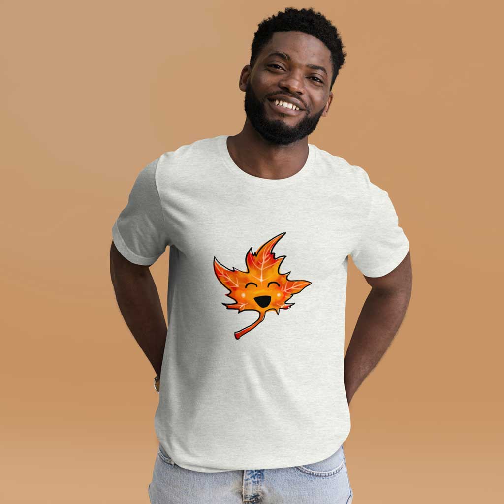 a person wears a t-shirt in the colour ash (very light grey) featuring a graphic of a smiling maple leaf