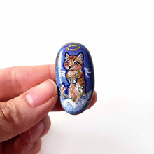 Load image into Gallery viewer, an oval shaped beach stone, hand painted with the portrait of an orange munchkin cat as an angel. standing up on clouds against a royal blue sky. available at a keepsake or pendant necklace
