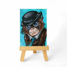 Load image into Gallery viewer, aceo sized painting of an orangutan with blue eyes, wearing a turquoise tie and black bowler hat, against a lighter turquoise background. the painting rests on a good easel
