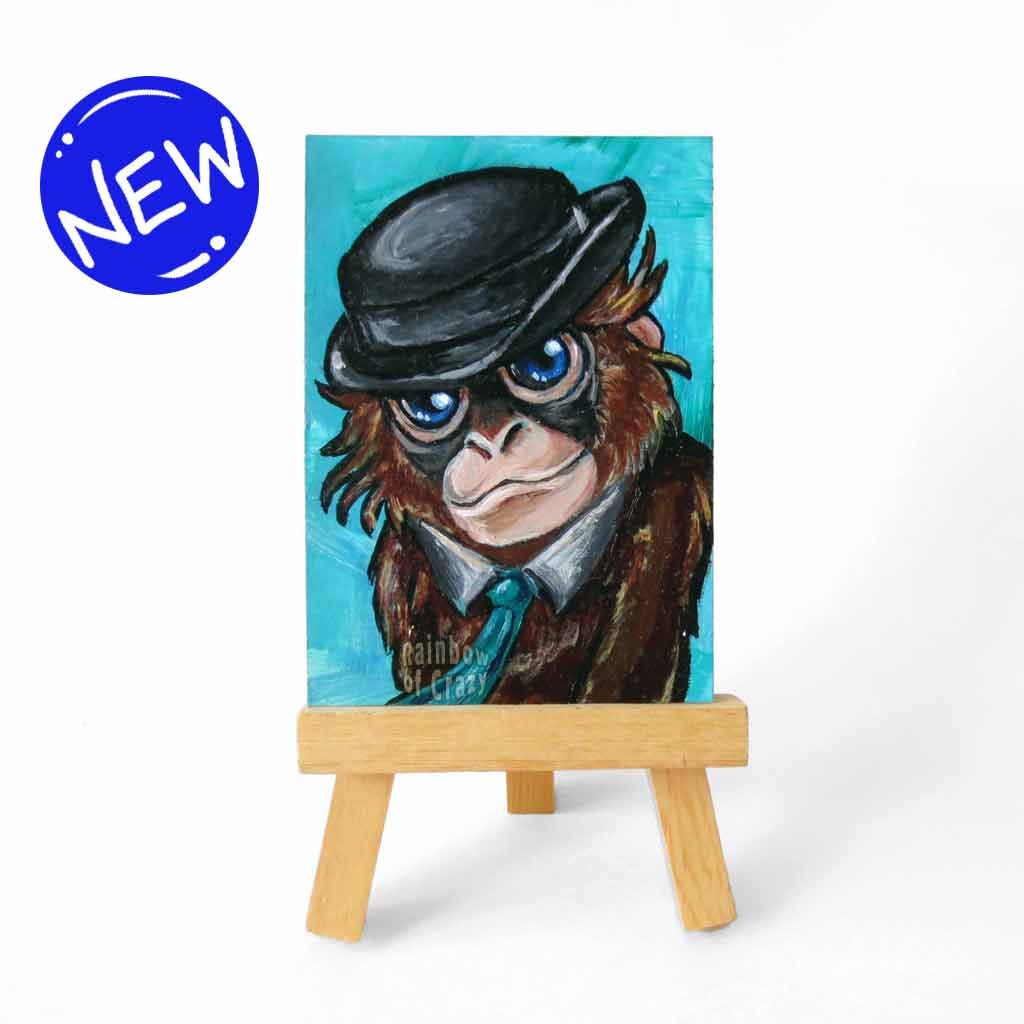 aceo sized painting of an orangutan with blue eyes, wearing a turquoise tie and black bowler hat, against a lighter turquoise background. the painting rests on a good easel