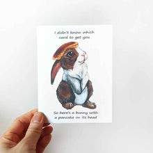 Load image into Gallery viewer, a greeting card, featuring an illustration of a brown and white rabbit with a pancake on its head. front reads, &quot;I didn&#39;t know which card to get you / So here&#39;s a bunny with a pancake on its head&quot;
