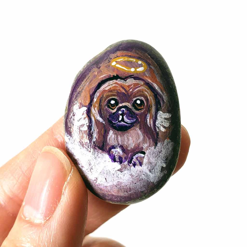 A portrait painting of a Pekingese dog as an angel with wings, painted on a small rock, available as a keepsake, fridge magnet, or pendant necklace