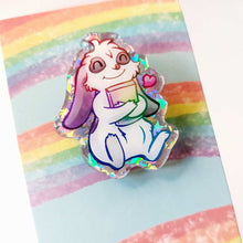 Load image into Gallery viewer, acrylic glitter pin featuring an illustration of a mini lop rabbit hugging a book, with a tiny heart next to him.
