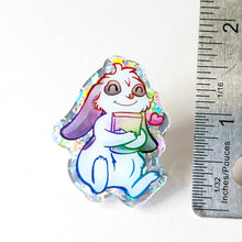 Load image into Gallery viewer, acrylic glitter pin featuring an illustration of a mini lop rabbit hugging a book, with a tiny heart next to him.
