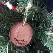 Load image into Gallery viewer, back view of wood ornament hanging on a christmas tree, painted to look like a pepperoni pizza, signed with RainbowofCrazy, with a small slice of pizza next to the name
