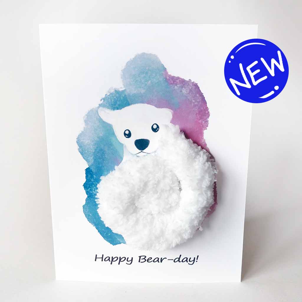 a greeting card with an illustration of a polar bear. thick, fluffy white yarn makes up the bear's body. the background has a splash of blue and purple. the front says, 