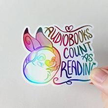 Load and play video in Gallery viewer, holographic sticker with a smiling rabbit wearing headphones. the sticker reads, "Audiobooks count as reading"
