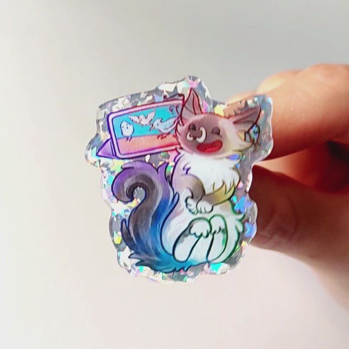 hand gently tilting an acrylic pin of a smiling ragdoll cat watching birds on a tablet to show the glitter effect