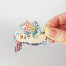 Load and play video in Gallery viewer, A clear, rainbow holographic acrylic keychain featuring a character from Rainbow of Crazy Comics: a smiling mini lop rabbit lounges on his back as he reads a book with a picture of a rabbit on the back.
