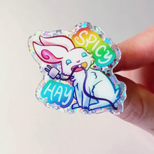 Load and play video in Gallery viewer, sparkly acrylic pin of a smiling white rabbit holding a charging cable in her mouth, with the words "SPICY HAY in rainbow colours.
