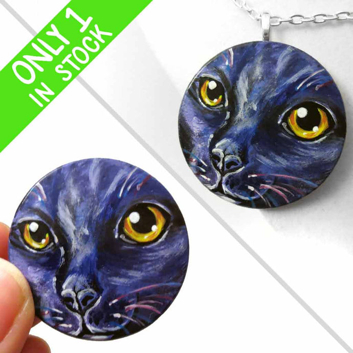 A wood disc painted with the portrait of a cat in dark purple and black, available as a keepsake or pendant necklace