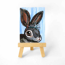 Load image into Gallery viewer, an aceo sized painting featuring a close up of a rabbit wearing a sparkling tiara, background painted a light blue. the painting sits on a tiny wood easel
