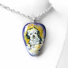 Load image into Gallery viewer, a beach stone hand painted with a sheepdog, as an angel with a halo, sitting on clouds against a purple and yellow sky. available as a keepsake or pendant necklace
