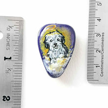 Load image into Gallery viewer, a beach stone hand painted with a sheepdog, as an angel with a halo, sitting on clouds against a purple and yellow sky. available as a keepsake or pendant necklace
