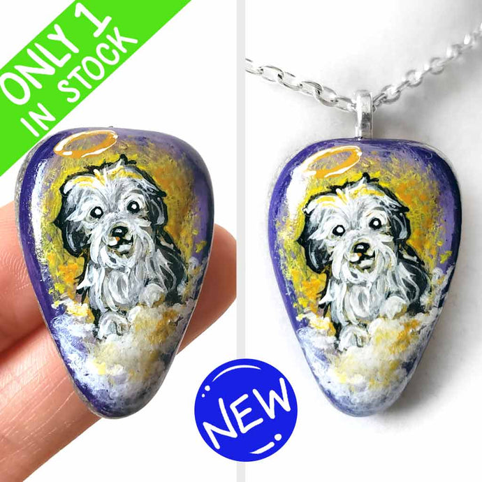 a beach stone hand painted with a sheepdog, as an angel with a halo, sitting on clouds against a purple and yellow sky. available as a keepsake or pendant necklace