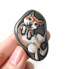 Load image into Gallery viewer, small beach stone, hand painted with a portrait of a shiba inu dog, lying on its back, belly up, tongue blopping out. available as a keepsake rock art or pendant necklace
