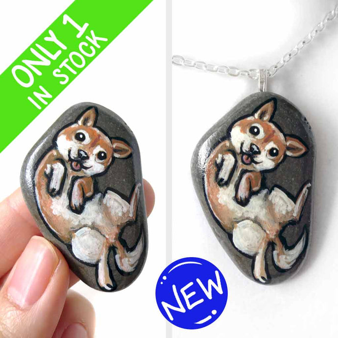 small beach stone, hand painted with a portrait of a shiba inu dog, lying on its back, belly up, tongue blopping out. available as a keepsake rock art or pendant necklace