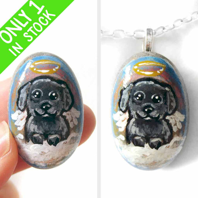 A small beach stone, hand painted with a portrait of a black shih tzu dog as an angel sitting in the clouds. Available as a keepsake or necklace