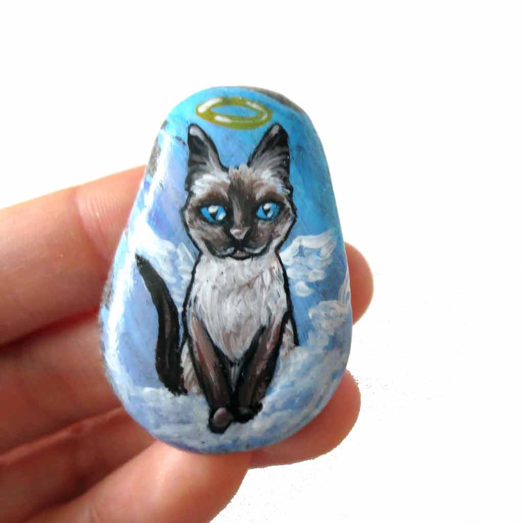 art of a siamese cat as an angel, is hand painted on a river rock, and is available as either a keepsake, fridge magnet,
 or a pendant necklace
