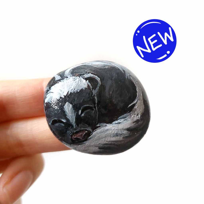 a small beach stone, painted to look like a sleeping baby skunk