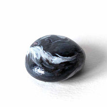 Load image into Gallery viewer, a small beach stone, painted to look like a sleeping baby skunk

