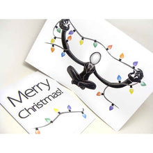 Load image into Gallery viewer, a greeting card with outside text: &quot;Merry Christmas!&quot; with a string of lights beneath / Inside features an illustration of Slender Man sitting cross-legged, arms out stretched, holding a long line of christmas lights
