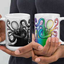 Load image into Gallery viewer, one hand holding a 15 oz white ceramic mug with an illustration of Slender Man forming a heart with his hands. a second hand is holding a second mug, showing it from the other side, featuring the same illustration, mirrored, in all the colours of the rainbow.
