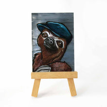 Load image into Gallery viewer, aceo sized painting on a wood easel, features a sloth wearing a navy blue flat cap hat, against a gray background
