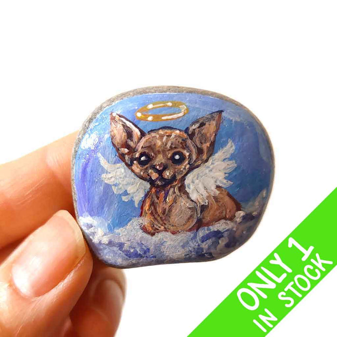 a beach stone, hand painted with a portrait of a sphynx cat, painted as an angel with halo and wings, sitting on fluffy clouds