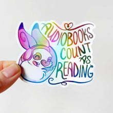 Load image into Gallery viewer, holographic sticker with a smiling rabbit wearing headphones. the sticker reads, "Audiobooks count as reading"
