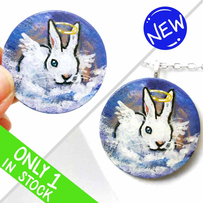 a wood disc, hand painted with the portrait of a white rabbit with blue eyes, painted as an angel, with halo and wings, sitting on clouds against a blue sky. available as a keepsake or pendant necklace