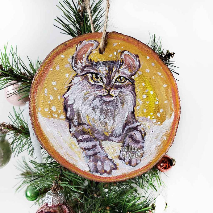 A wooden ornament with art of an American Curl cat with golden eyes, watching the snow fall