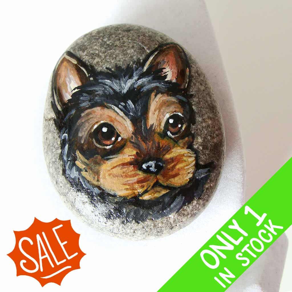 a beach stone, hand painted with the portrait of a black and brown yorkie's face