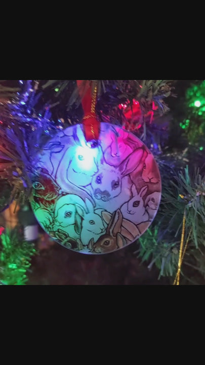 a round glass ornament, printed with a collage of different rabbit breeds, hanging from a Christmas tree with a red ribbon and gold string
