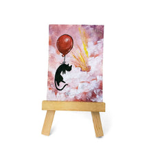 Load image into Gallery viewer, An original ACEO painting, on an easel, of a black cat with a red balloon, floating  through the clouds in the sky, painted with reds and purples. 
