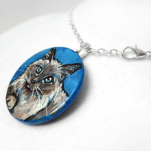 Load image into Gallery viewer, a wooden pendant necklace painted with a portrait of a birman cat with blue eyes, on a blue background
