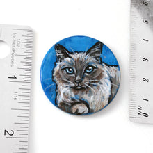 Load image into Gallery viewer, a circle shaped wooden disc, hand painted with a brown and white birman cat with blue eyes. the piece is next to two rulers to show its size: 1 1/2 inches or 3.8 cm across
