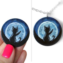 Load image into Gallery viewer, A lightweight wooden disc features art of the silhouette of a black cat, with a front paw reaching up, sitting in front of a big glowing full moon. Available as a keepsake or necklace
